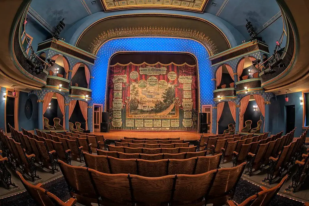 Stoughton Opera House - a historic theater with ornate decorations, wooden seats, and a colorful painted stage curtain featuring various advertisements and scenic illustrations. , The Goose Crown Inn