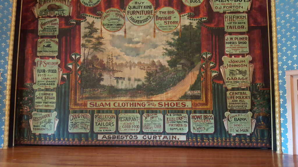 Stoughton Opera House interior view of the stage with house curtain showing old-time business promotions from around Stoughton; the Goose Crown Inn