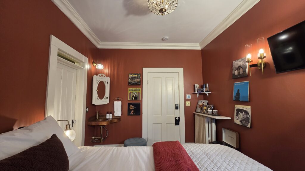 Stoughton inn guest room with copper sink, queen bed in foreground, a record player and vinyl LPS; the Goose Crown Inn