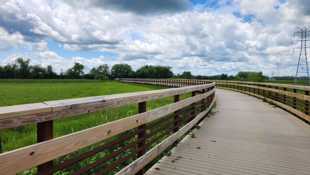 Boardwalk path curves through a green meadow on the Lower Yahara River Trail - hiking near Stoughton - the Goose Crown Inn